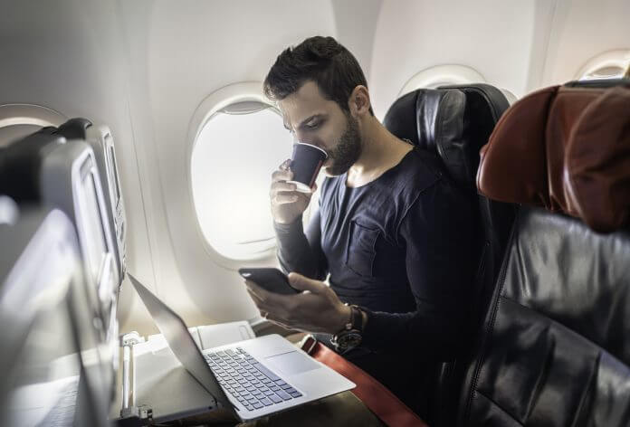 Man working in airplane using cellphone and drinking coffee